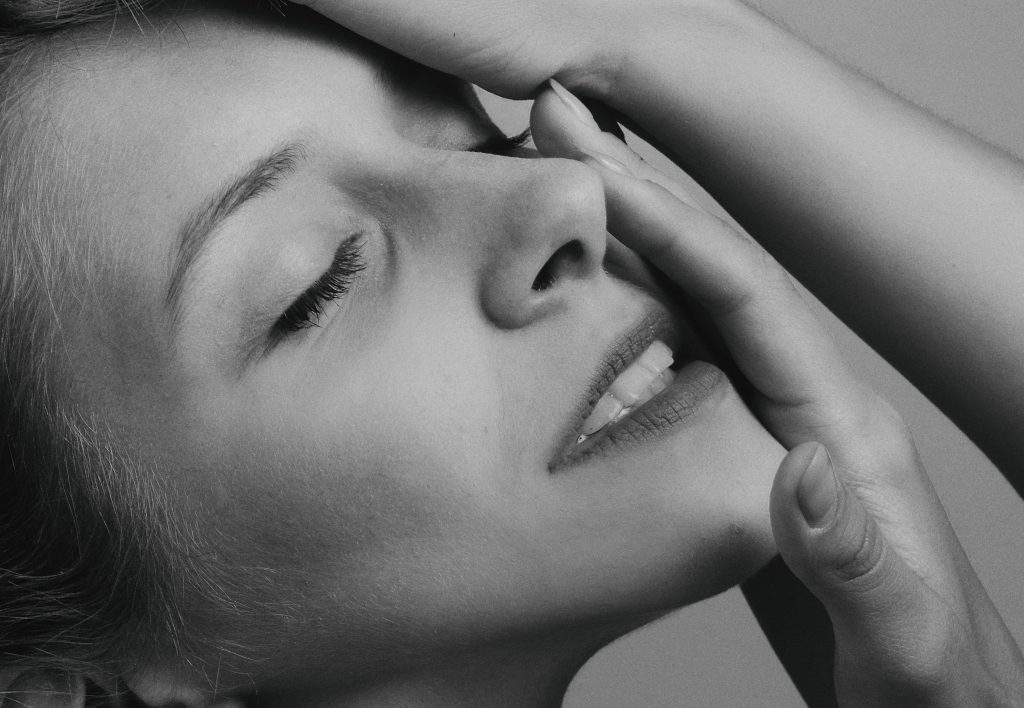 Close up of black and white image of a woman's face with her eyes closed and her hand resting on one side of her face.
