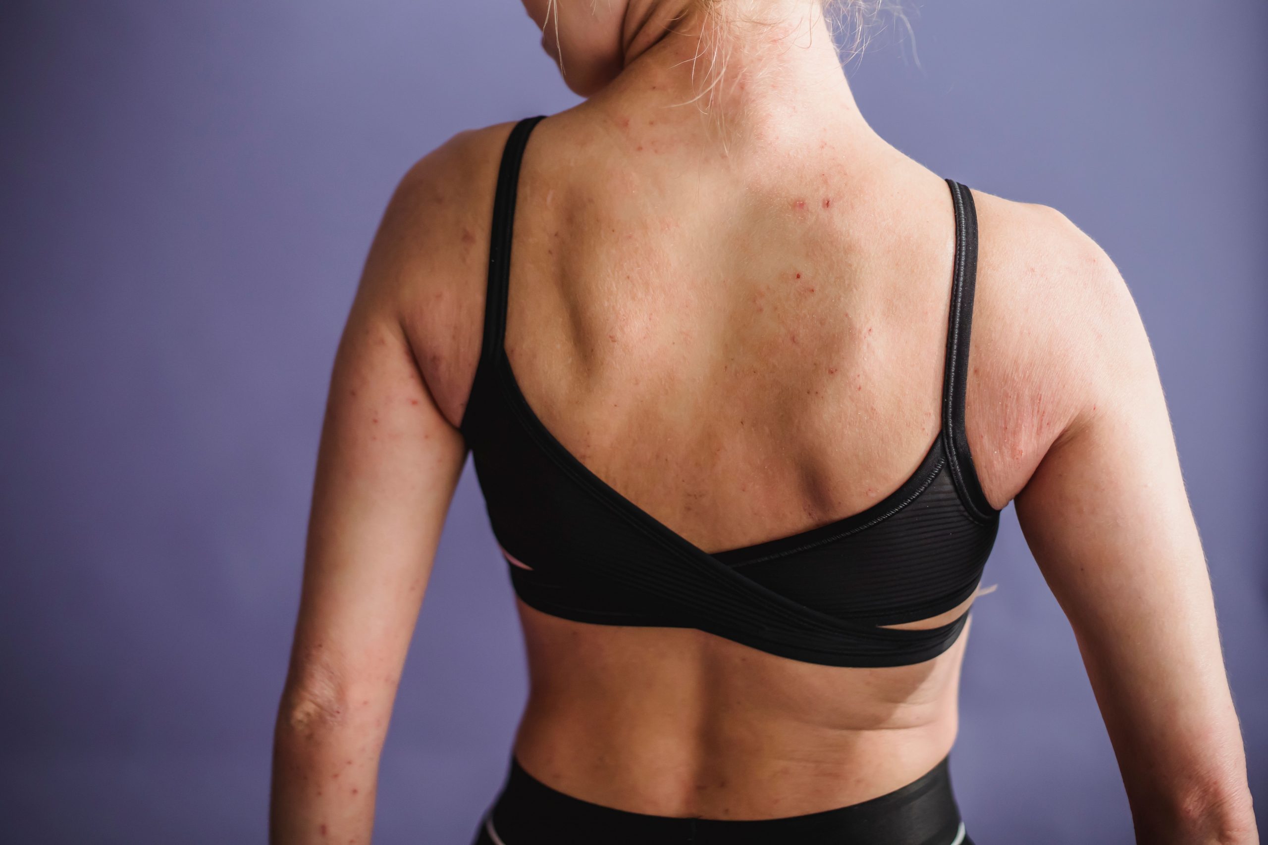 A back view of a woman's body from the waist up to the neck. The woman is wearing a black bra and pants, and the image shows her looking over her shoulder.
