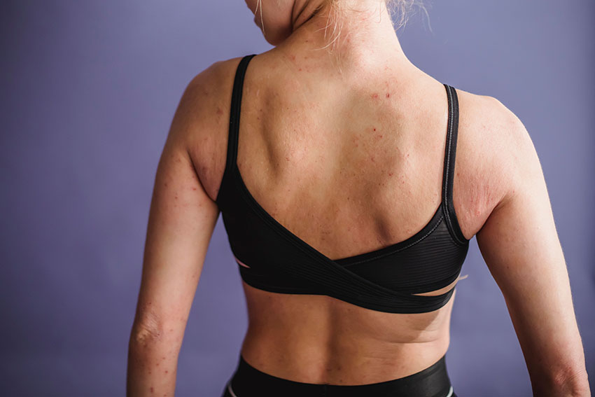 A back view of a woman's body from the waist up to the neck. The woman is wearing a black bra and pants, and the image shows her looking over her shoulder.
